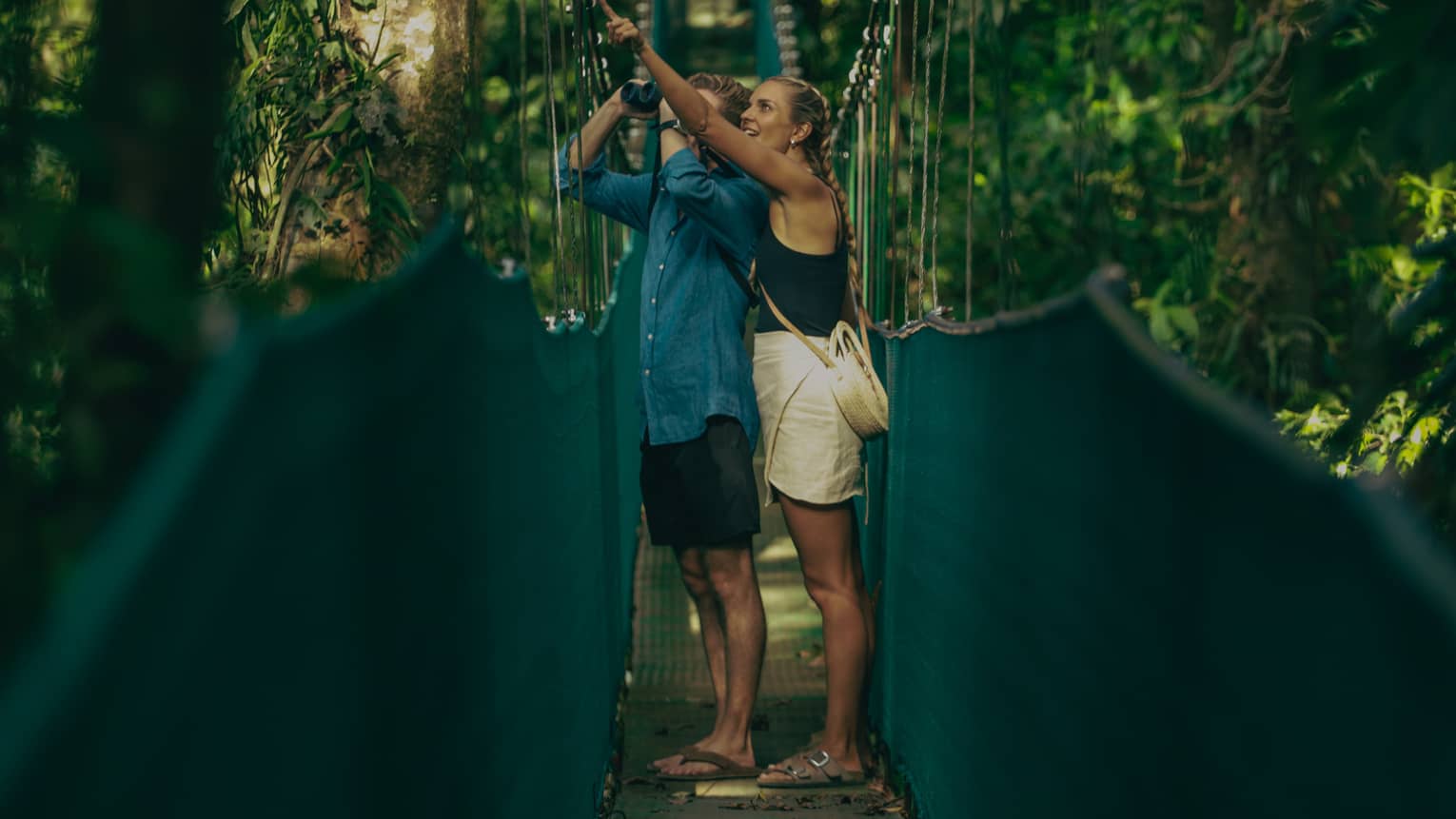 A man and woman walking along a hanging bridge.