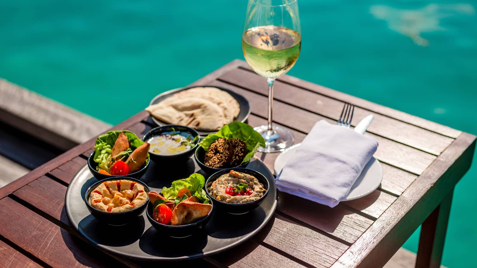 Arabic mezze platter and glass of white wine on poolside table