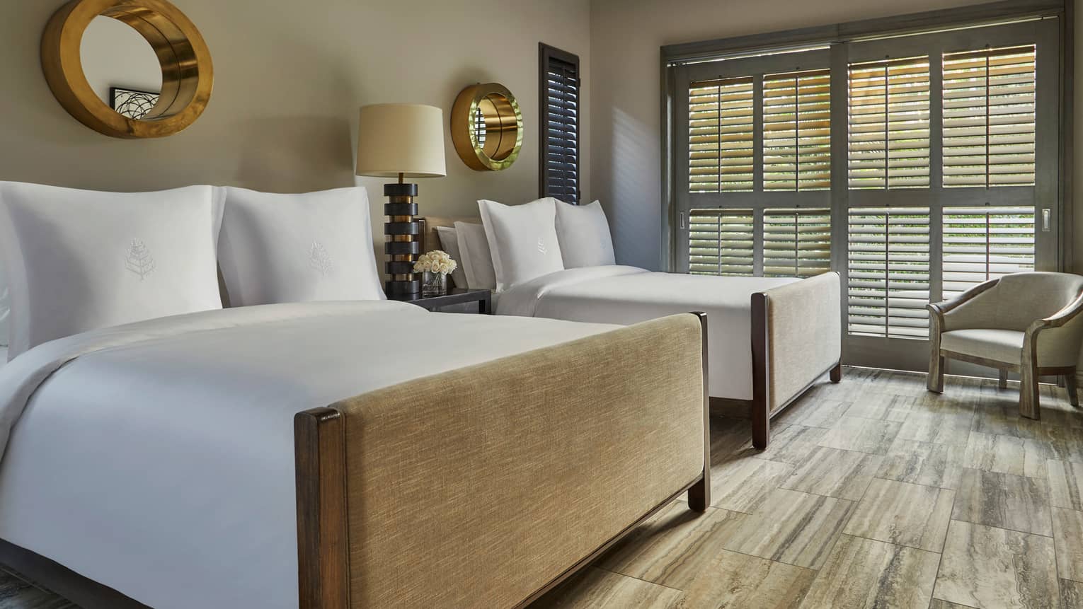 Two double beds in a serene guest room with wood floors, neutral tones and large shuttered windows