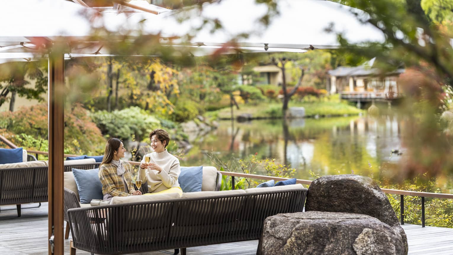 Two people sitting on an outdoor sofa, enjoying drinks by a tranquil pond garden at Four Seasons