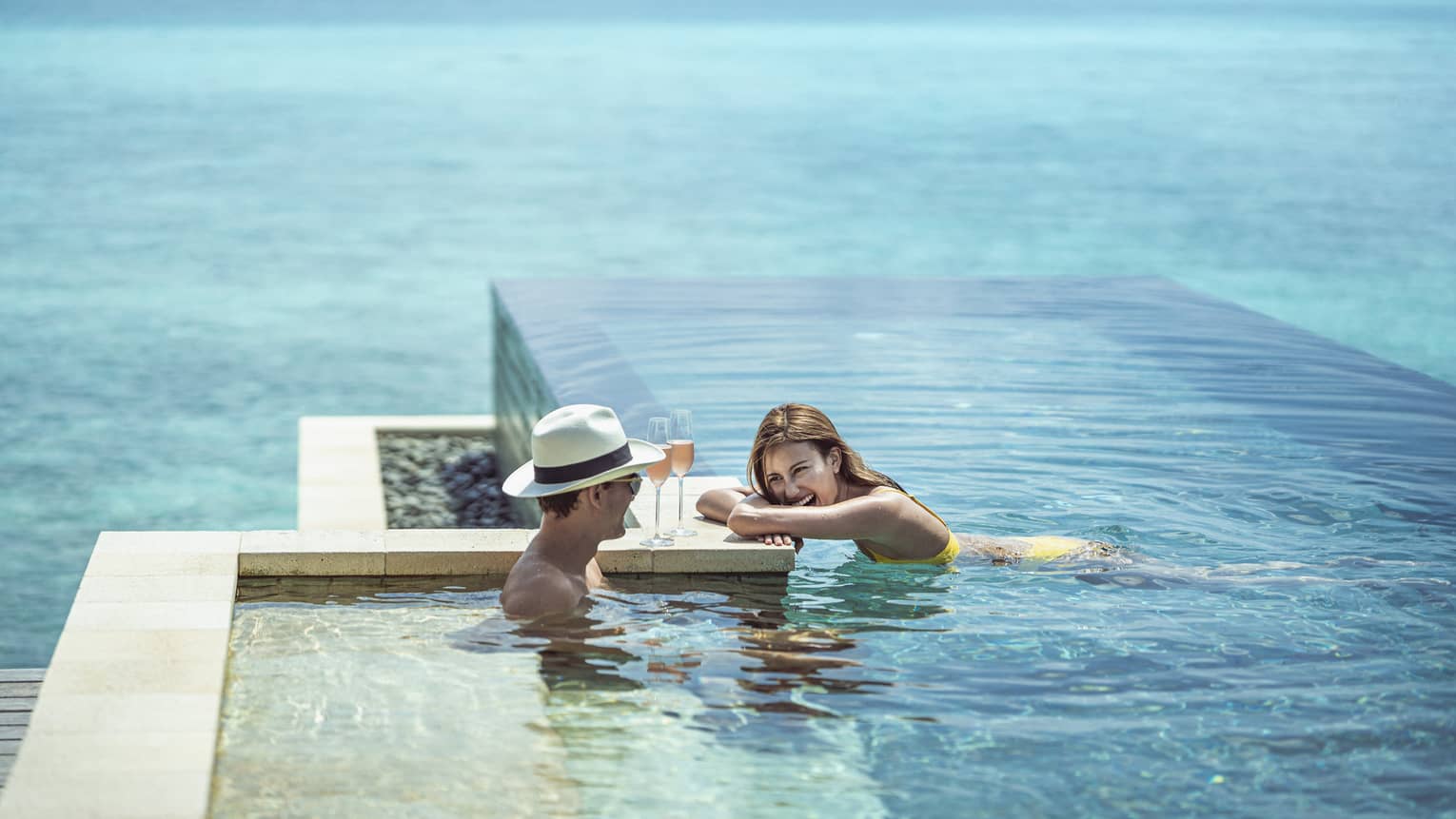 Couple relaxes with two glasses of wine in the infinity-edge pool