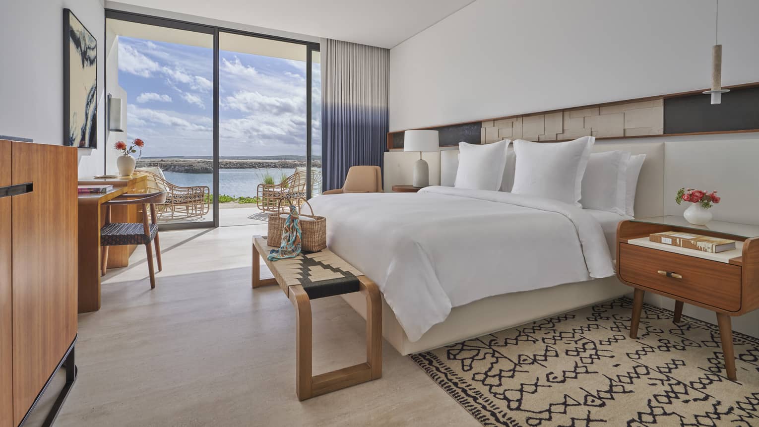 White bed with foot bench, side tables, tall glass doors and water views