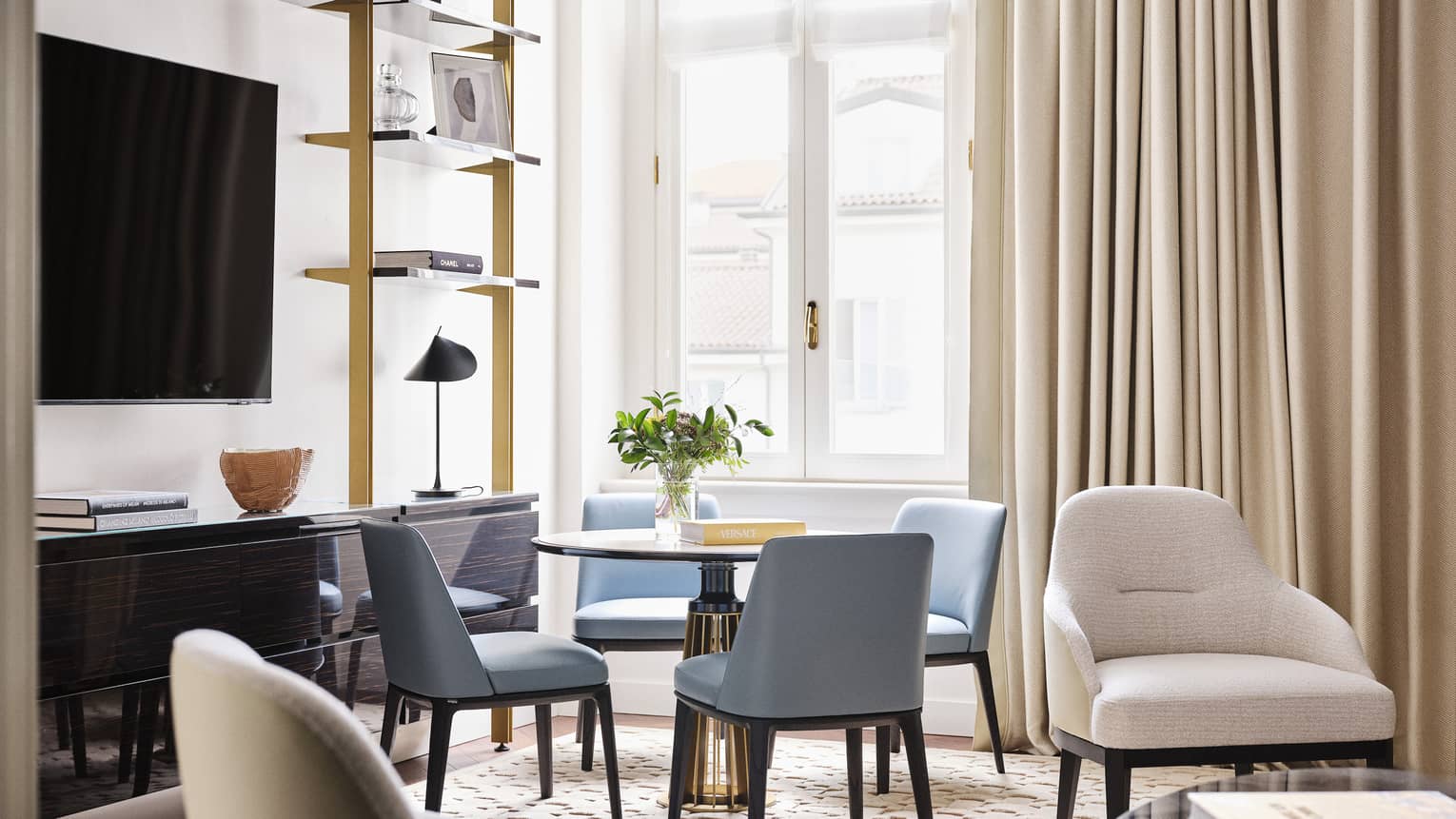 Contemporary living room of a hotel suite, featuring a round dining table with four blue chairs