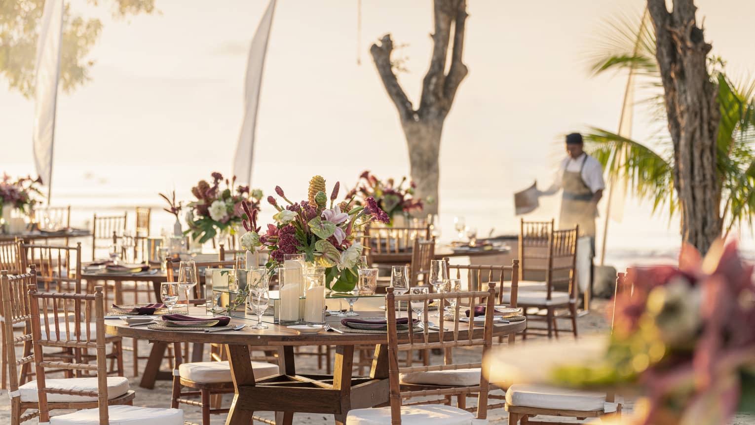 Beachside dinner setup with round tables and pink floral centrepieces