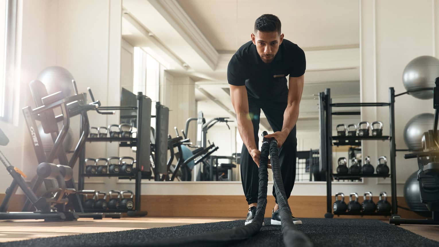Man works out in fitness room using a heavy rope