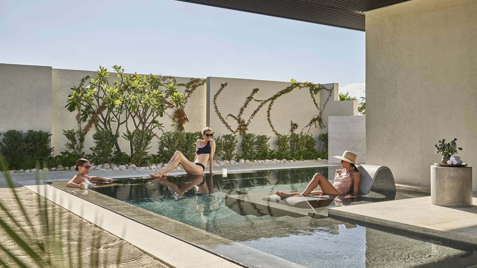 Three women lounging around a small outdoor pool.