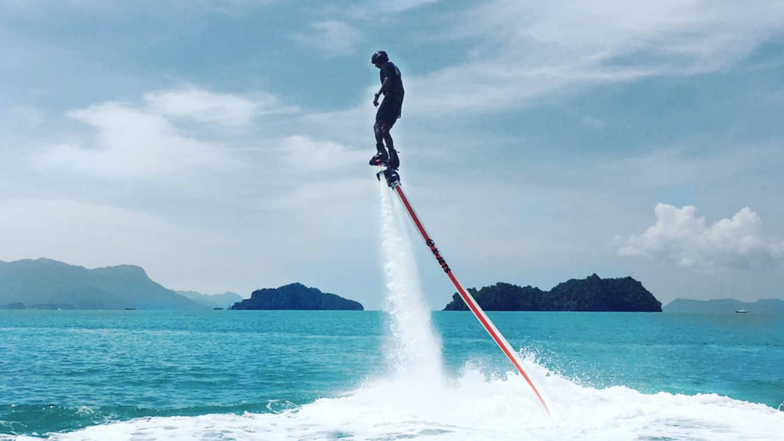 Water sprays as man soars above ocean attached to line, jet blade pack