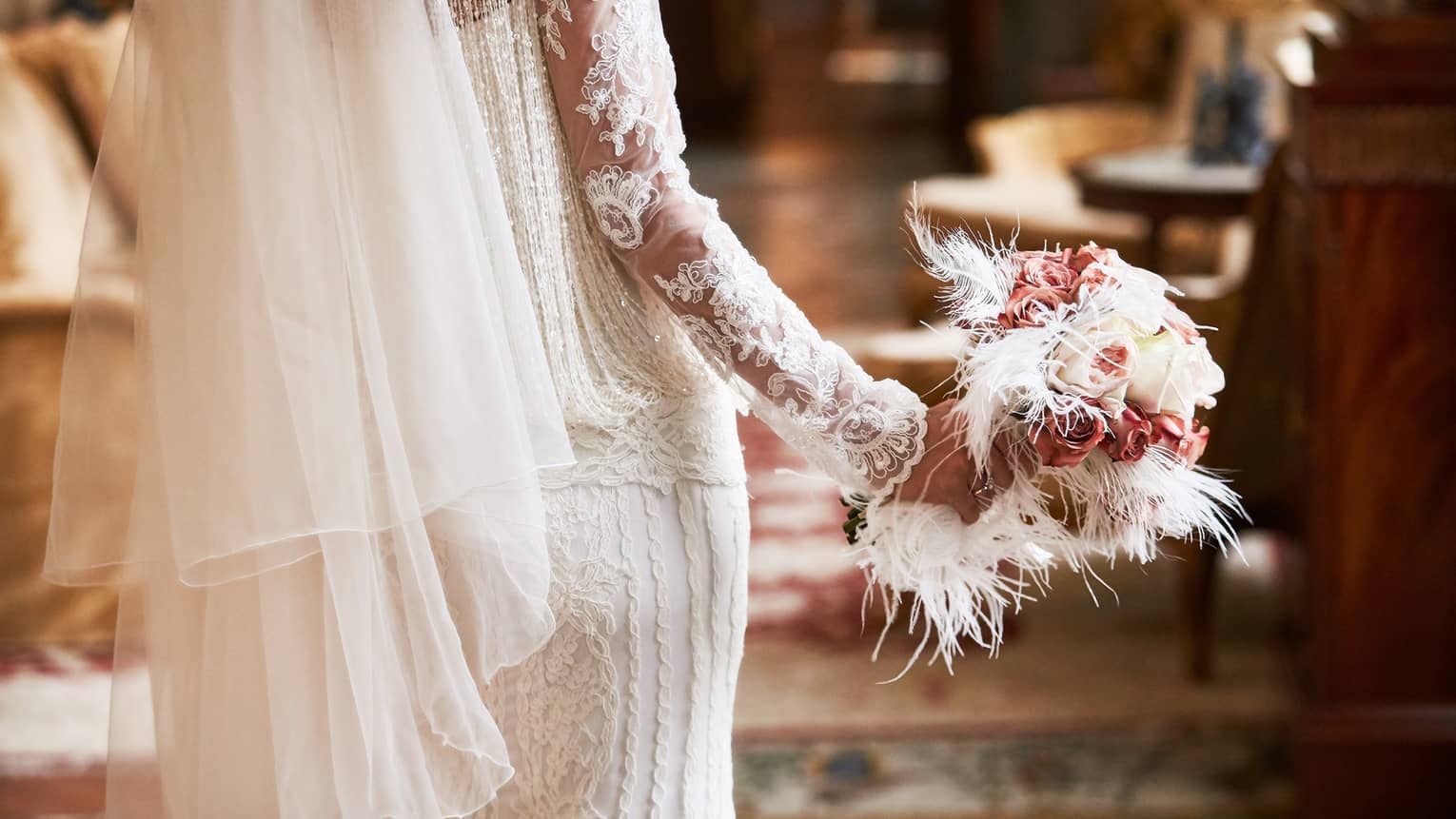 A close up of a bride's bouquet made up of white roses, pink flowers and white feathers
