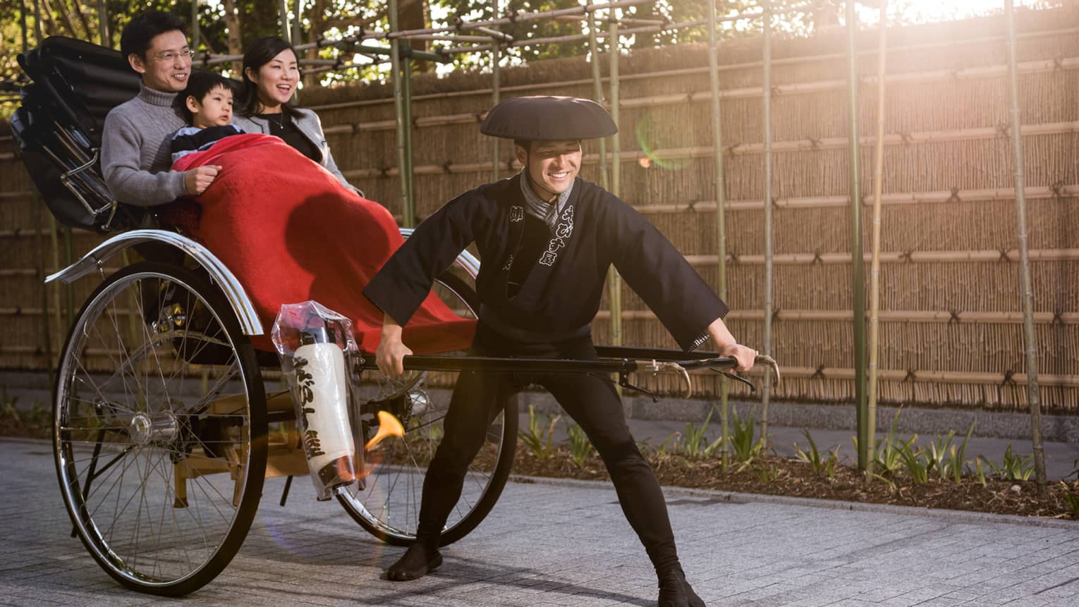 Couple, young boy under red blanket ride in rickshaw wagon pulled by man