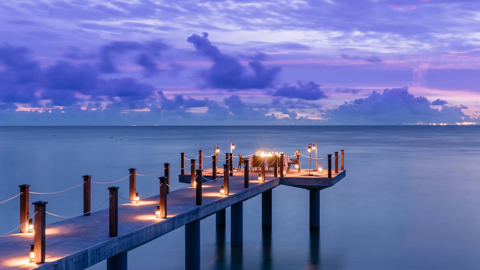 Candlelit jetty off Desroches Island with purple sunset hues