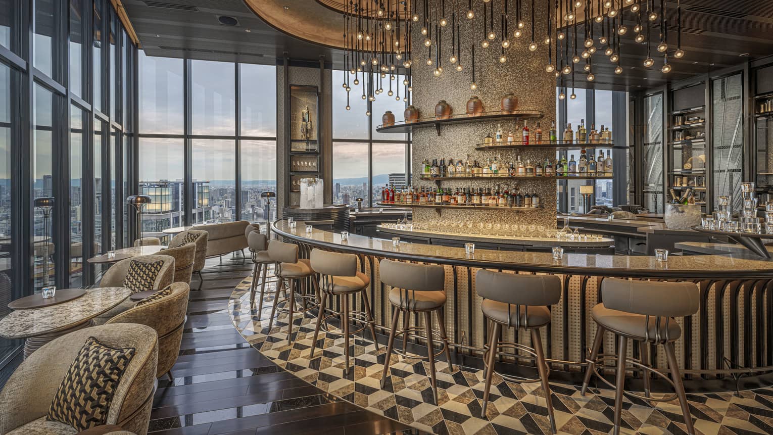Large circular granite-topped bar in a modern luxury restaurant surrounded by a bank of windows overlooking city at dusk.