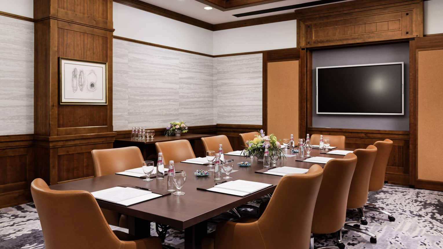 A meeting room with a long table, brown chairs and a screen on the wall.