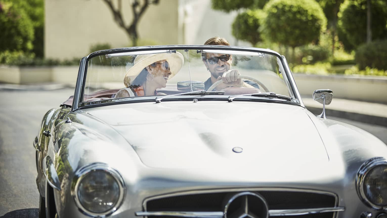 Smiling couple drive in silver luxury convertible car on sunny day