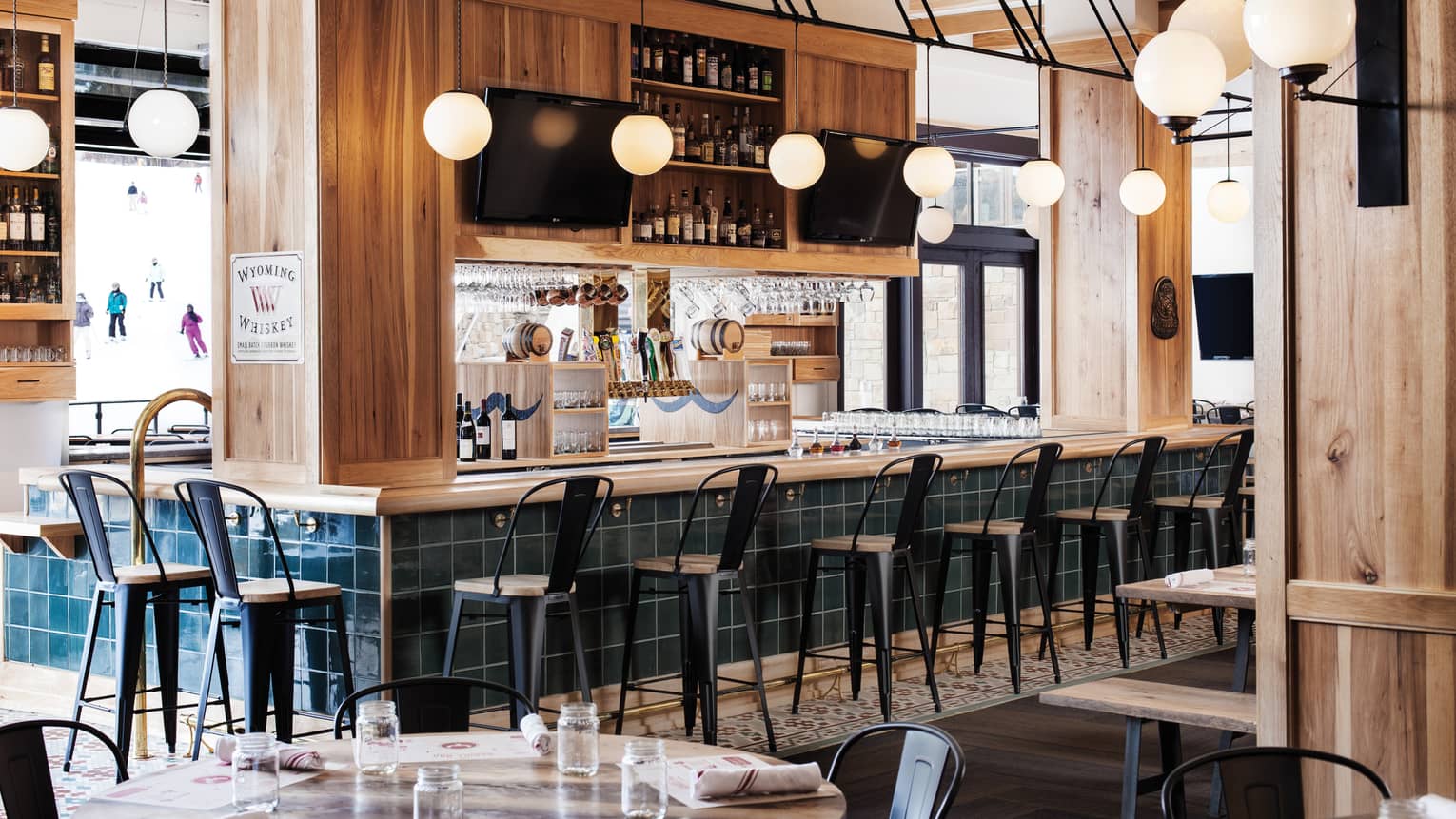 High chairs are positioned around a bar, bright windows show guests skiing outside 