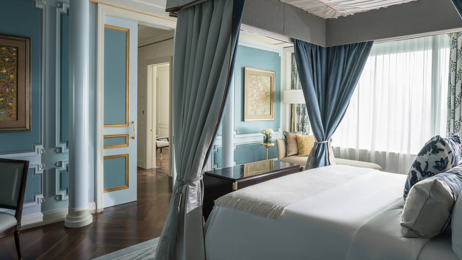 Canopy bed with white linens across from blue wall with pillar