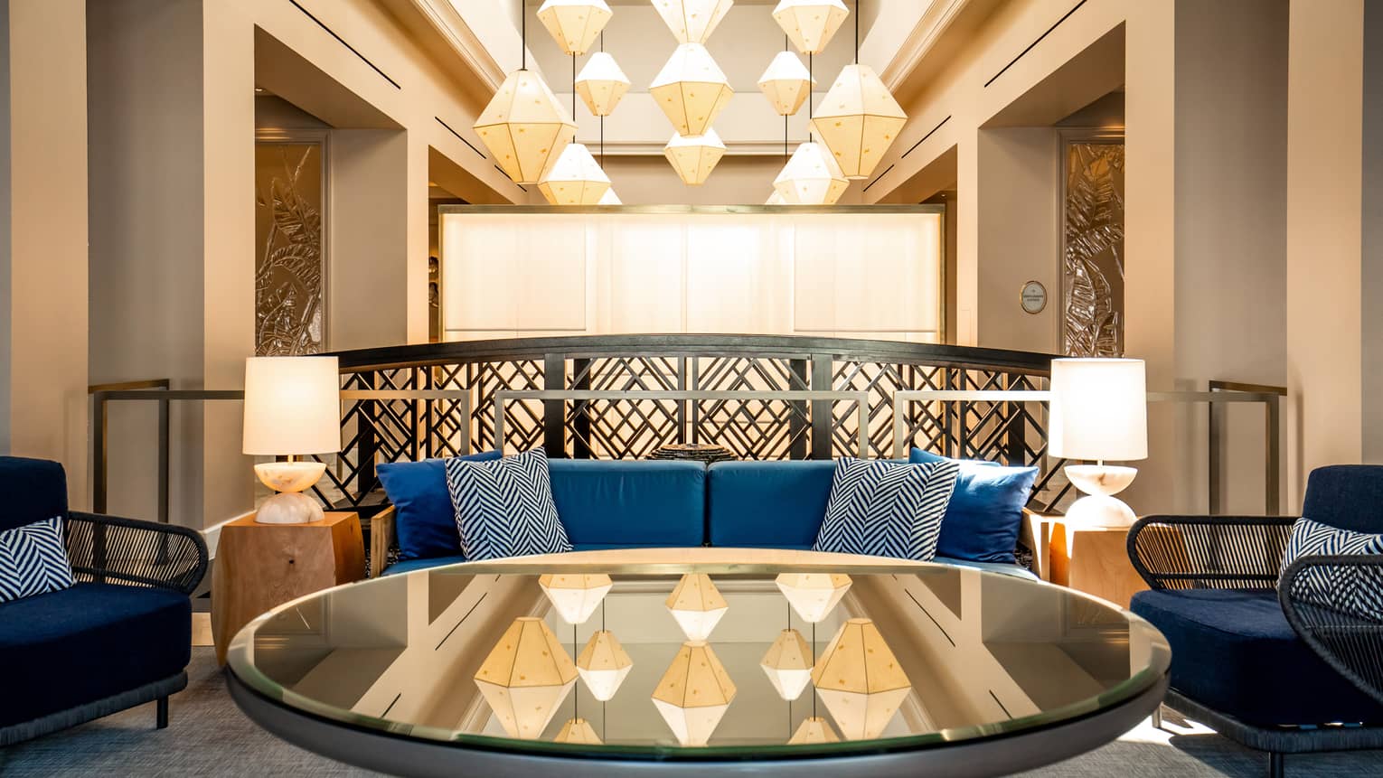 A lounge area with a geometric chandelier and blue sofas.