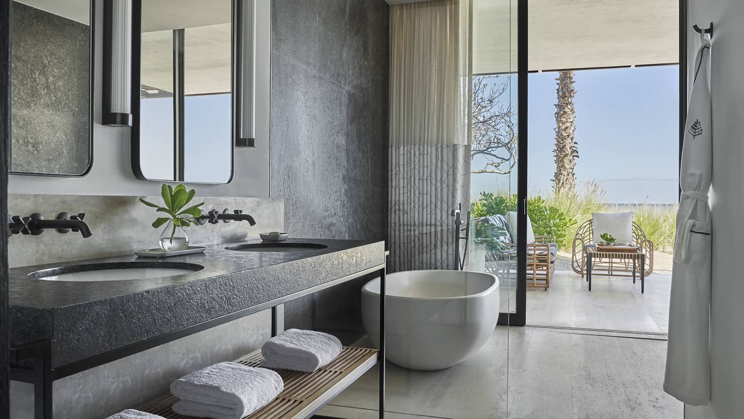 A bathroom with a large sliding glass door, bathtub, sink and towels on a shelf.