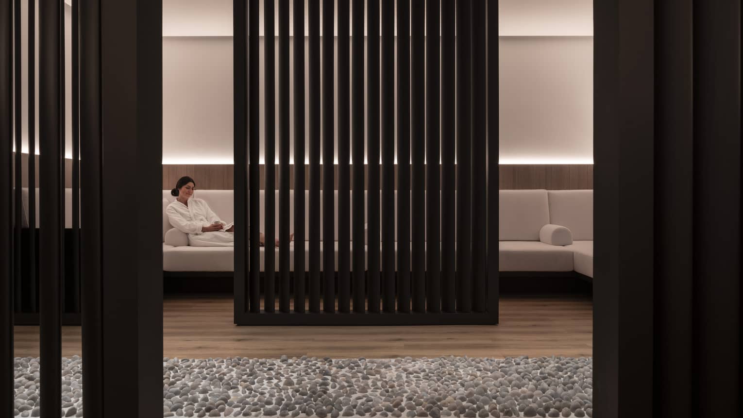 A woman lounges on a large white couch obscured by a black privacy wall. 