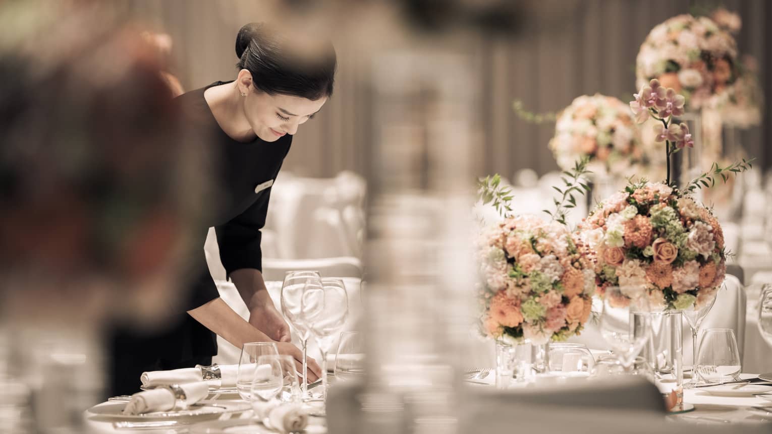 Hotel server sets formal banquet table with pink roses, flower arrangements