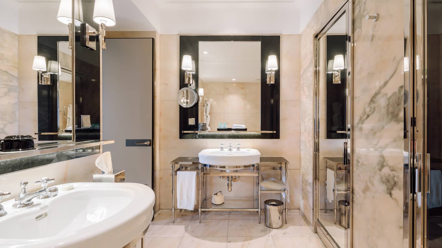 Modern bathroom with marble walls, dual sinks, large mirrors, wall-mounted lights and a glass-enclosed shower.