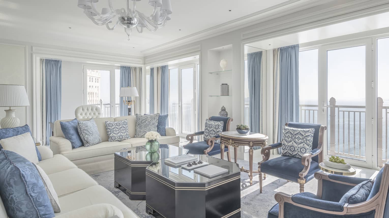 Living room with two white sofas, three blue arm chairs, blue curtains, two coffee tables