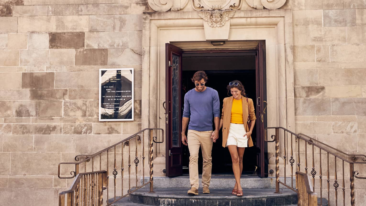 A man and woman walking out of an old stone building.