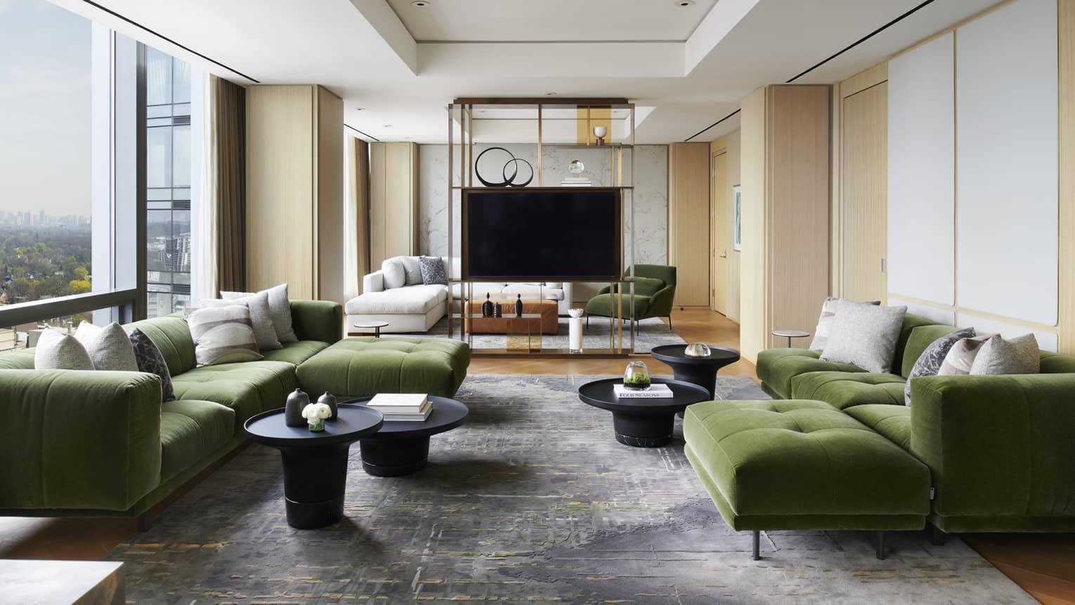 Living room with two large green velvet sofas, wall of windows, TV, grey area rug