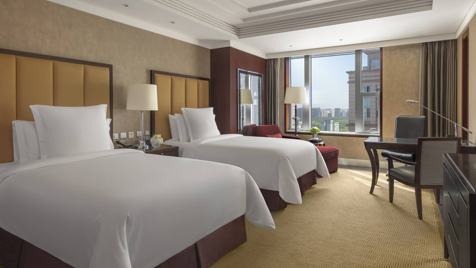 Hotel room with two single beds, light brown walls, tan carpet, table with two chairs and window