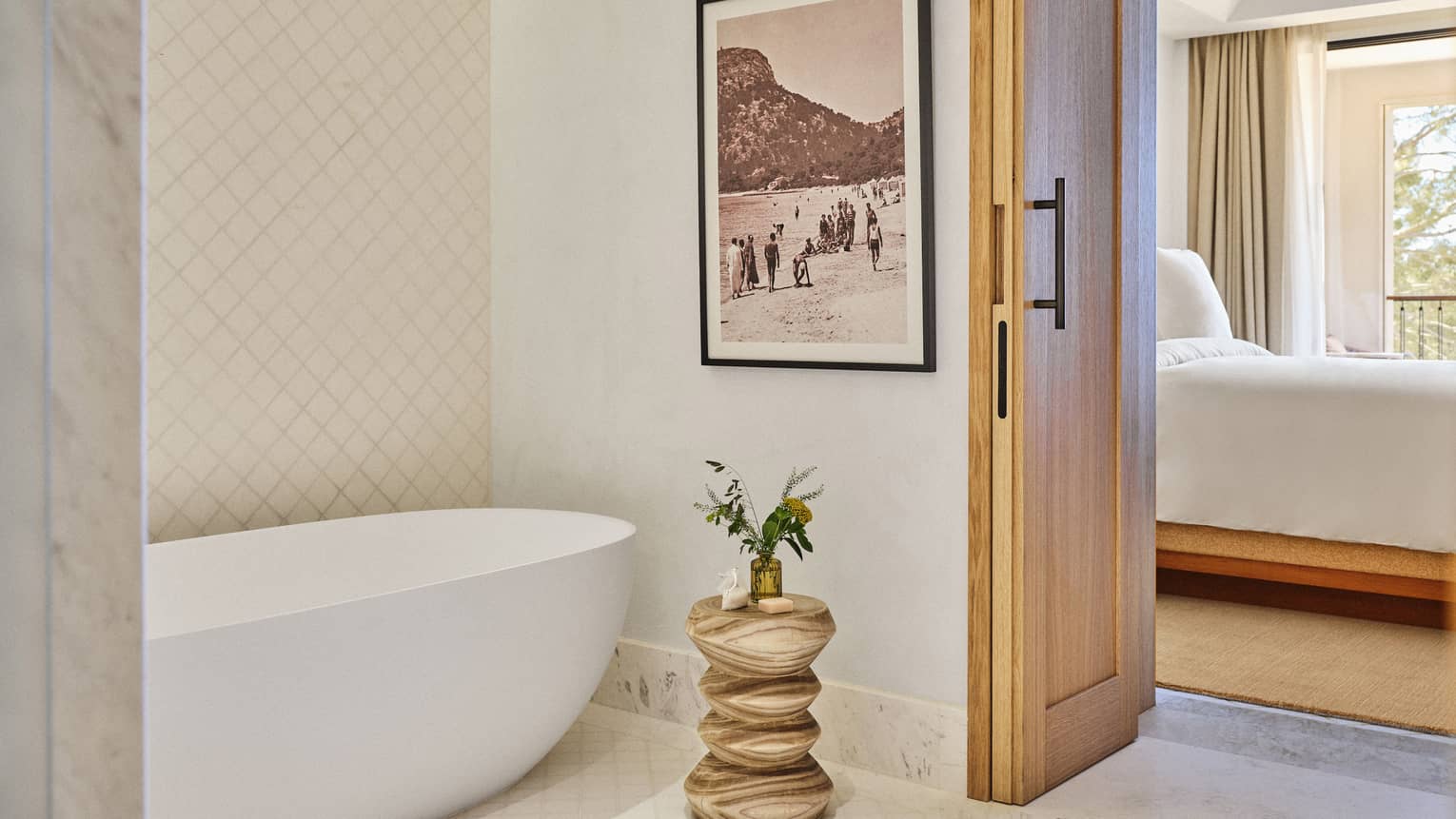 A luxury suite bathroom with standalone tub and modern wooden side table leading into bedroom at Four Seasons Resort Mallorca