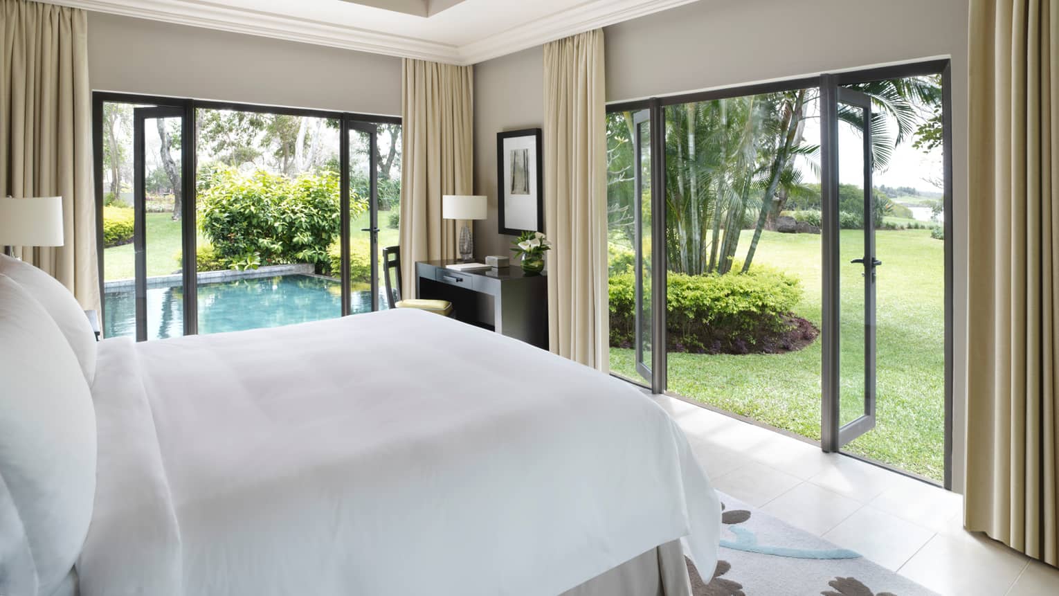 Deluxe Residence Villa side of bed with white linens, open corner patio doors, plunge pool
