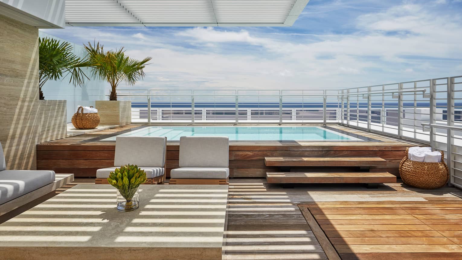 Luxury oceanfront penthouse terrace with a private pool, modern seating area, wooden deck and views of the ocean under a clear blue sky