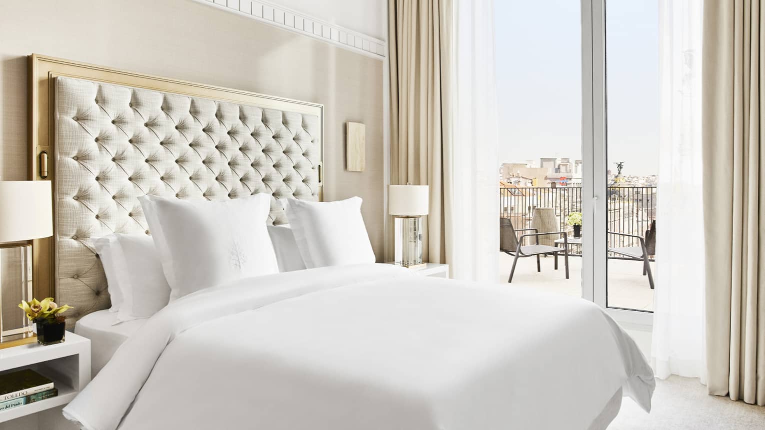 Luxury hotel suite bedroom with a king bed, tufted headboard, bedside lamps and access to a private terrace with city views
