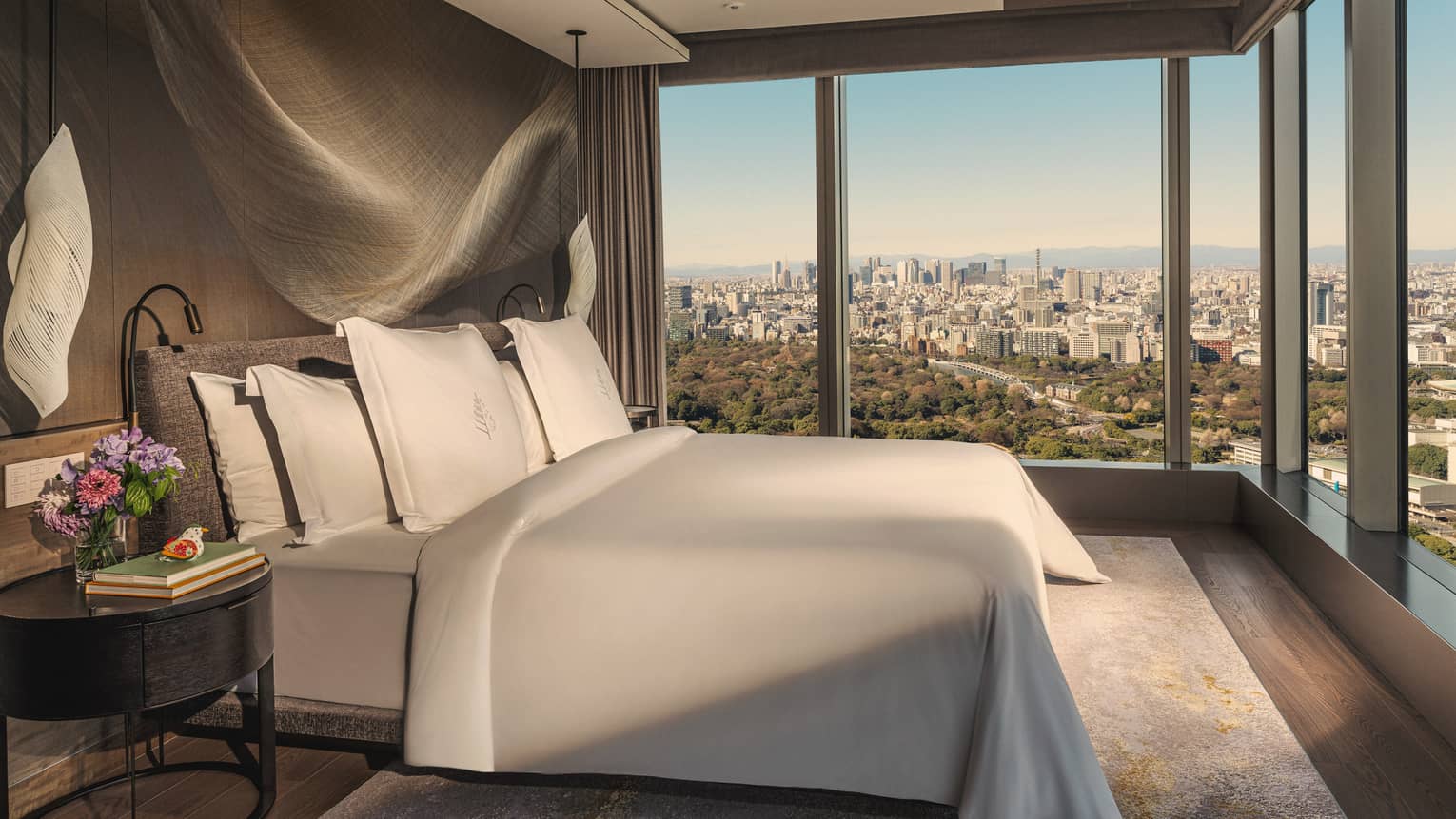Luxury hotel room with a king bed, modern hanging lighting fixtures, and two walls of windows
