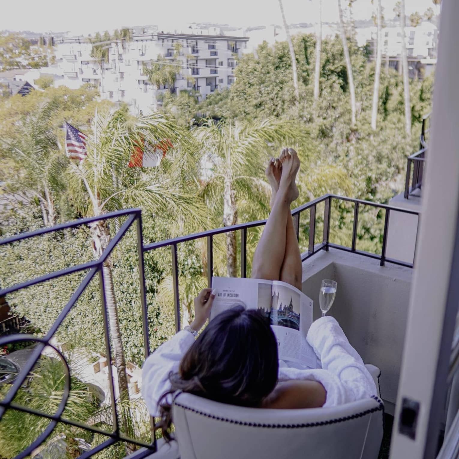 Woman sitting on balcony with champagne reading a magazine