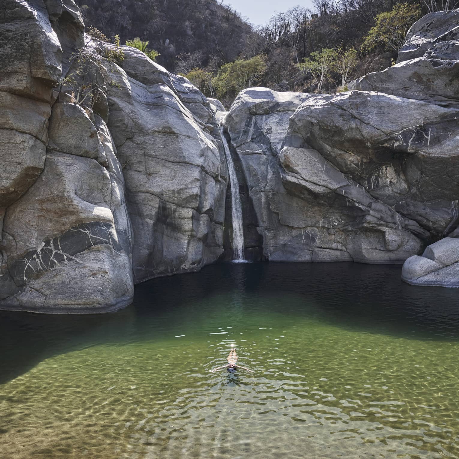 A person in a small well of water surrounded by large rock faces and trees.
