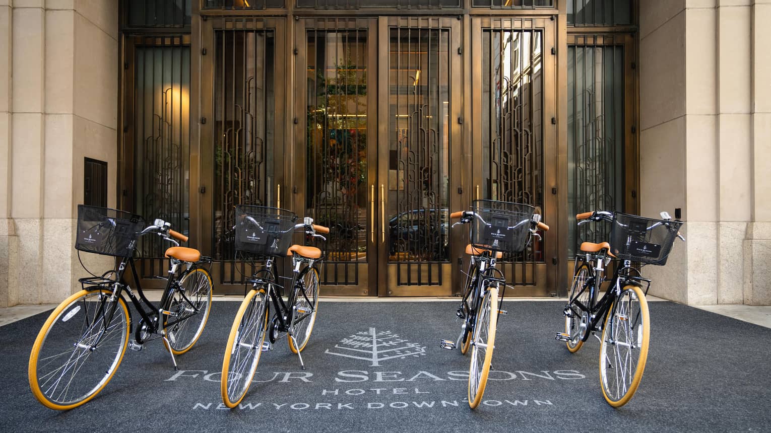 Four identical bicycles sit at the Hotel's exterior, the rug underneath displaying the Four Seasons logo