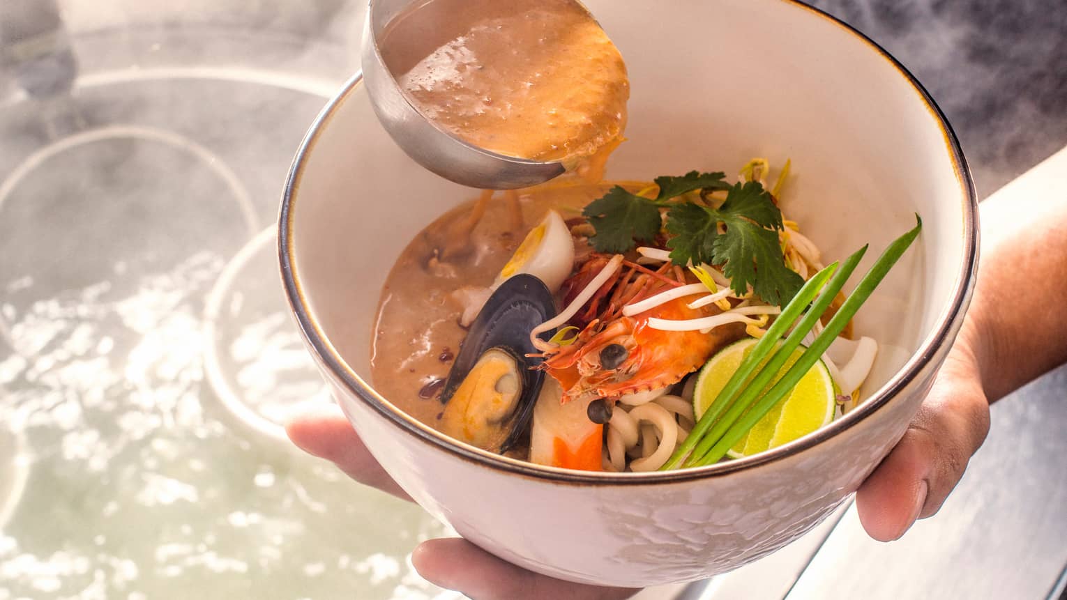 Close-up of hands holding Laksa Noodle seafood dish, ladle with sauce 