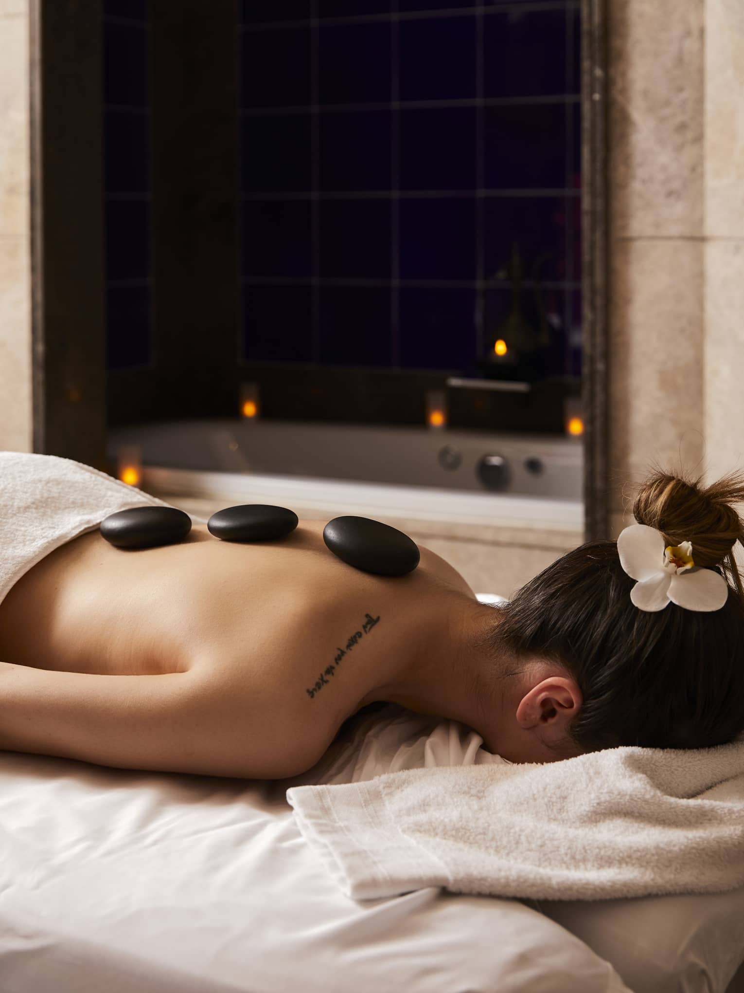Woman lays on spa massage table with three large stones along her spine