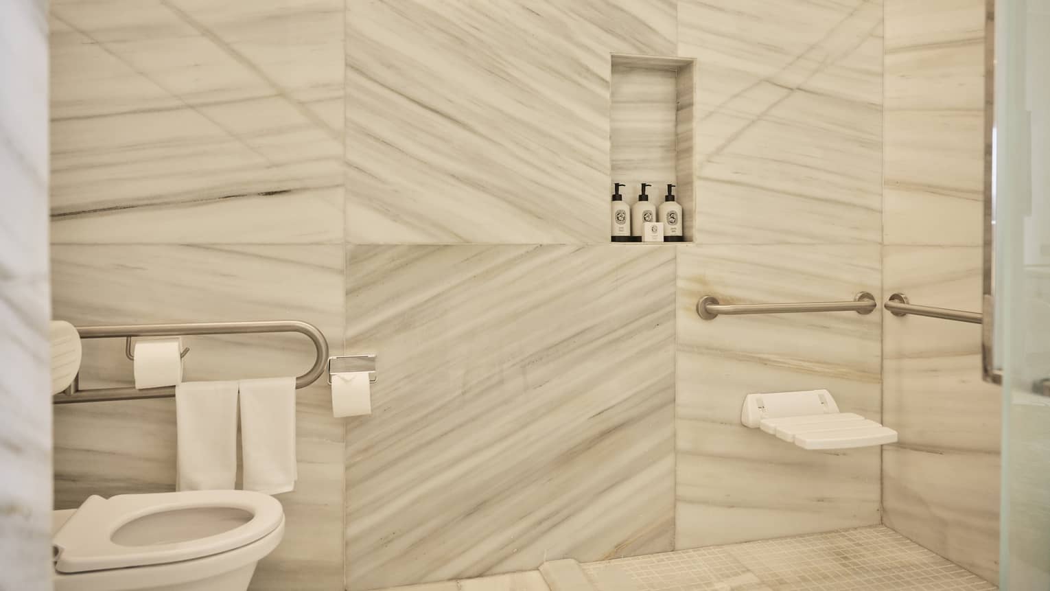 Mobility-accessible bathroom featuring marble walls and grab bars next to toilet and shower seat
