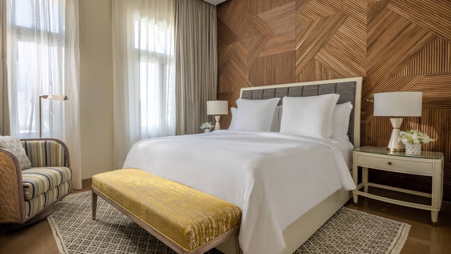 Guest bedroom with king bed and white linens, good foot bench, patterned armchair and area rug