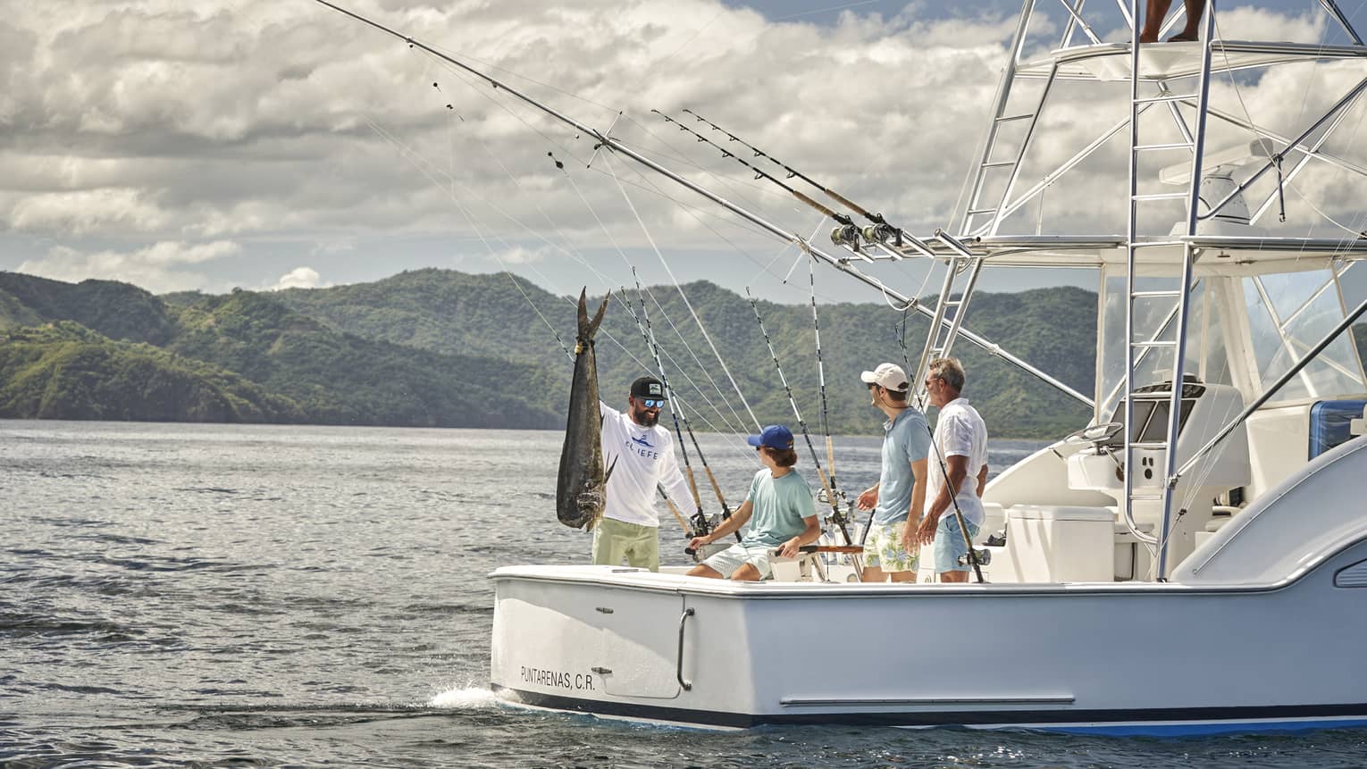 Four men are gathered on the back of a fishing boat with one of them holding a large fish up by the tail