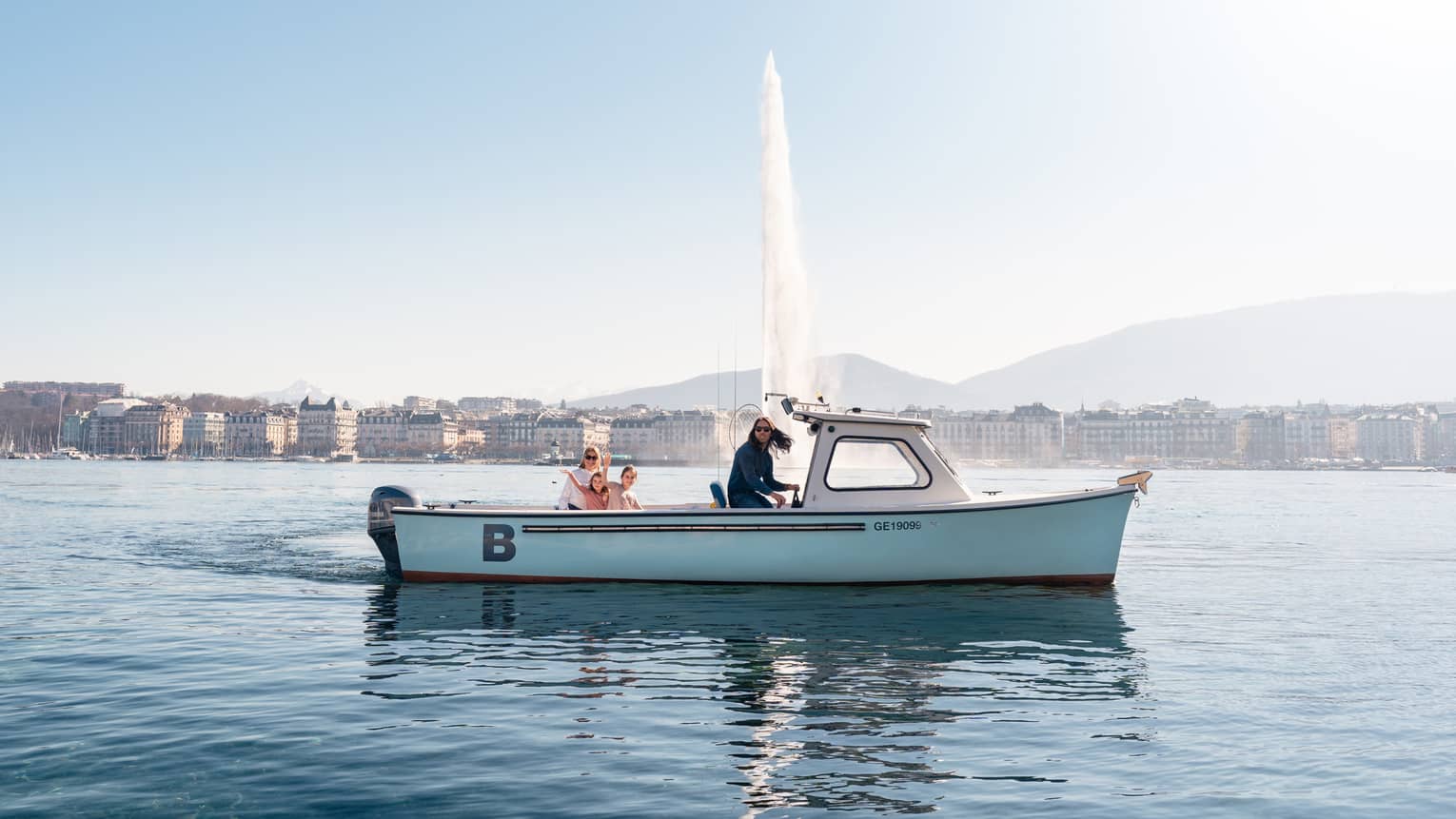 Four people in small boat on Lake Geneva with Jet d'Eau fountain and city in backdrop