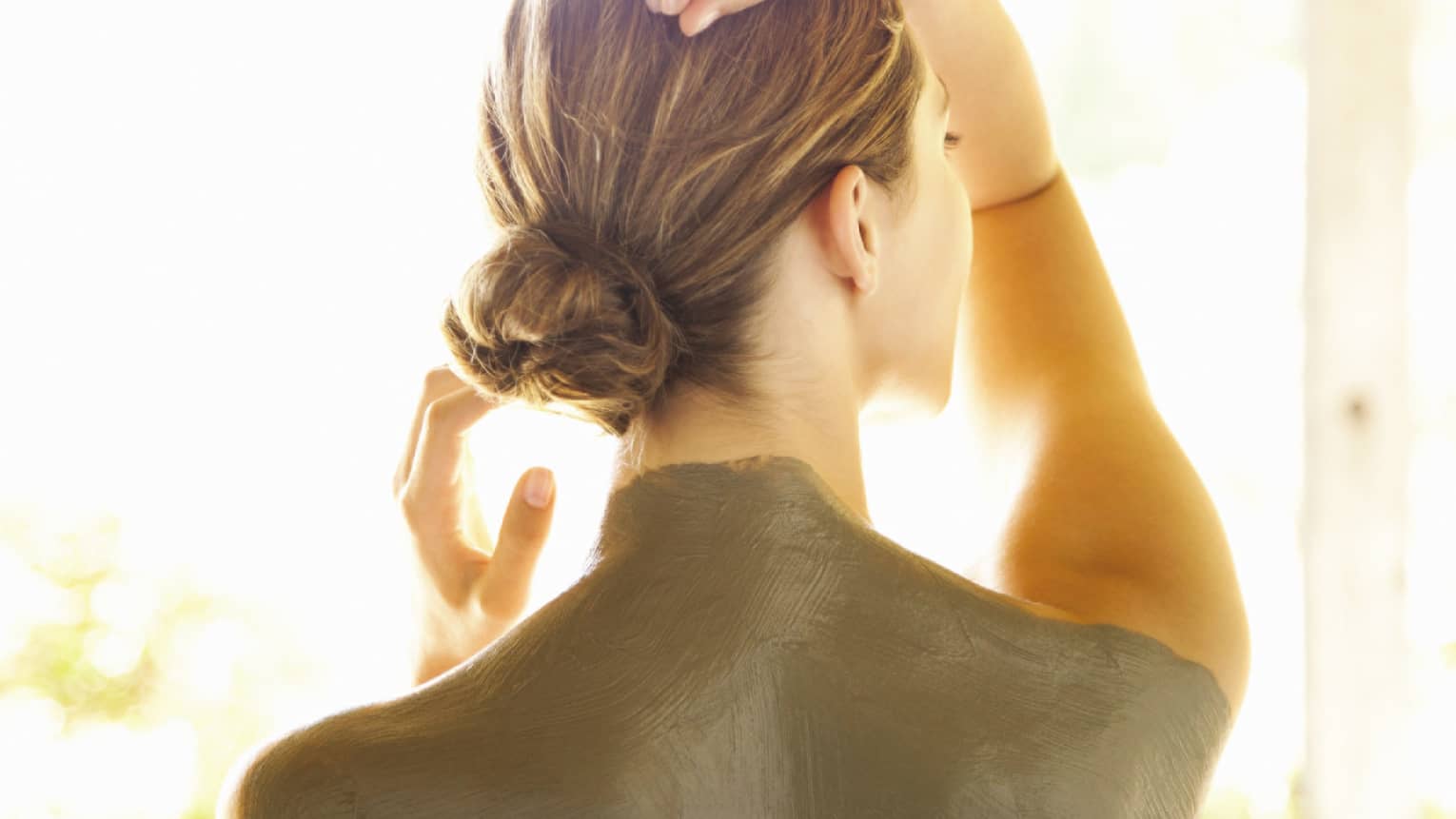 View of woman's back shoulders covered in dark green clay mud spa treatment
