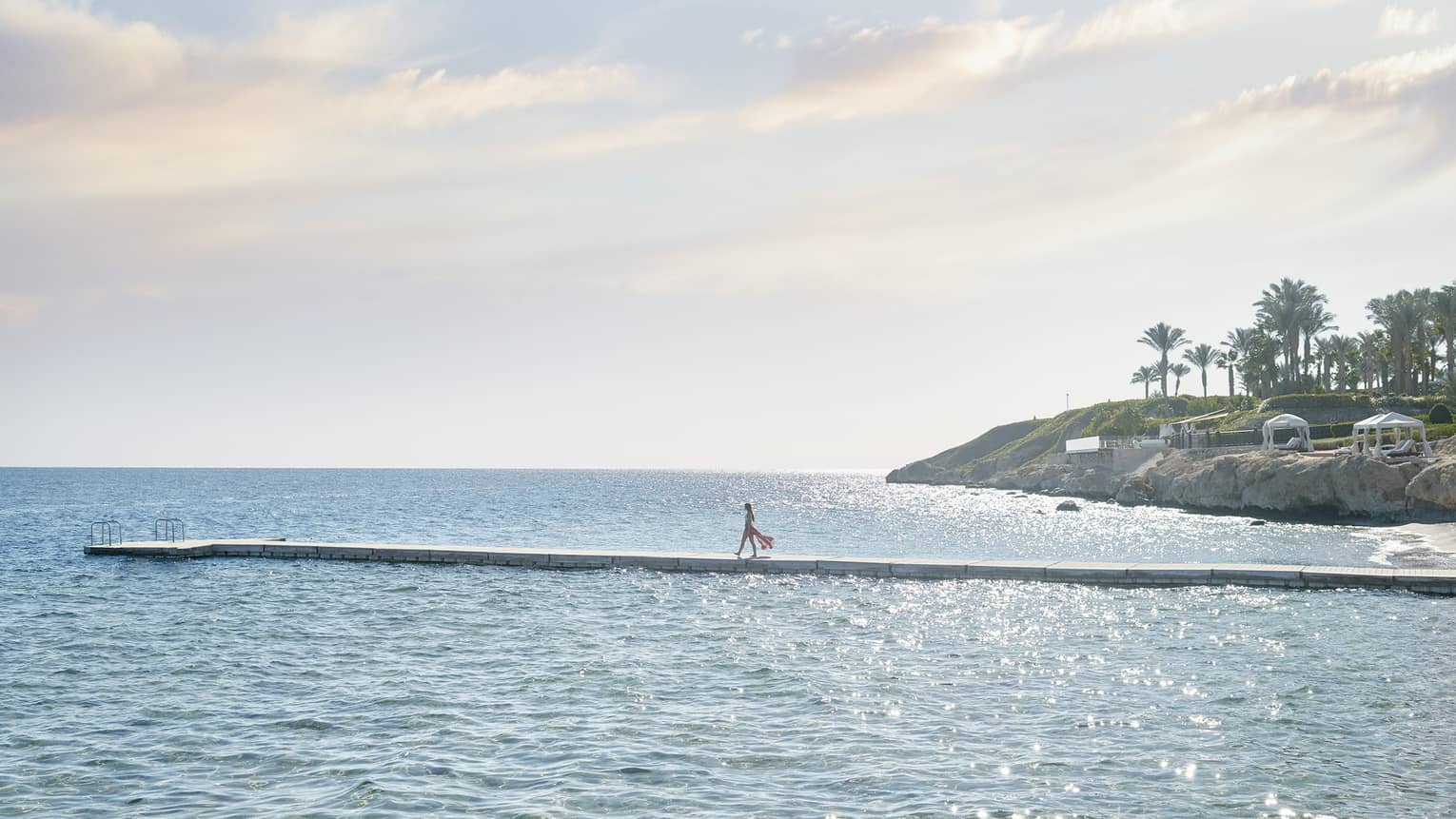Woman in flowing clothes walks on a long, narrow pier over the Red Sea at Four Seasons Resort Sharm El Sheikh
