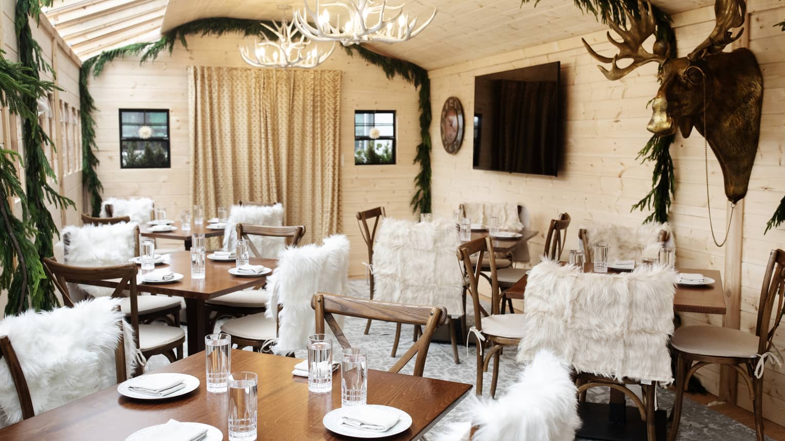 Many tables in a dining room with fur covers on the chairs and decorative garland.