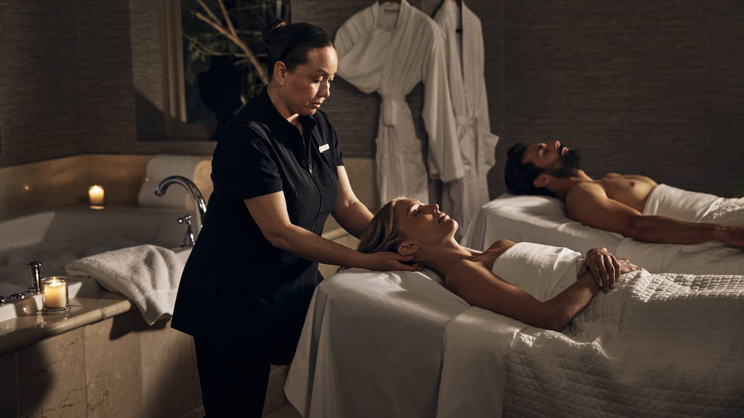 Two guests laying on massage tables in a room with a spa tub.