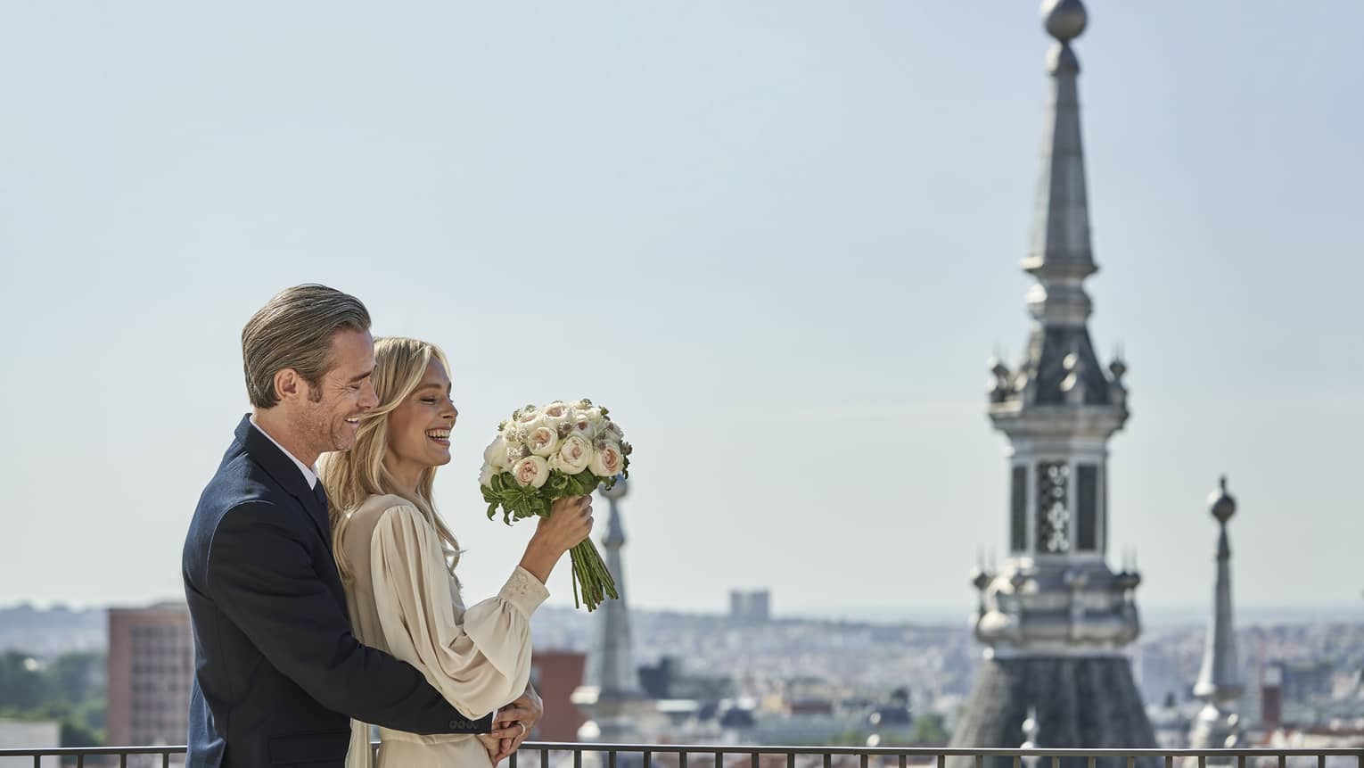 A couple embrace on a veranda overlooking several steeples in Madrid.