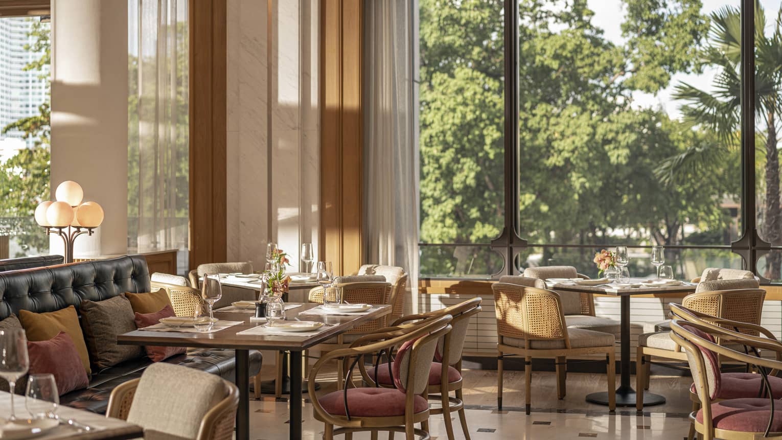 Riva restaurant with square tables set for four, comfortable chairs, floor-to-ceiling windows with natural lighting 