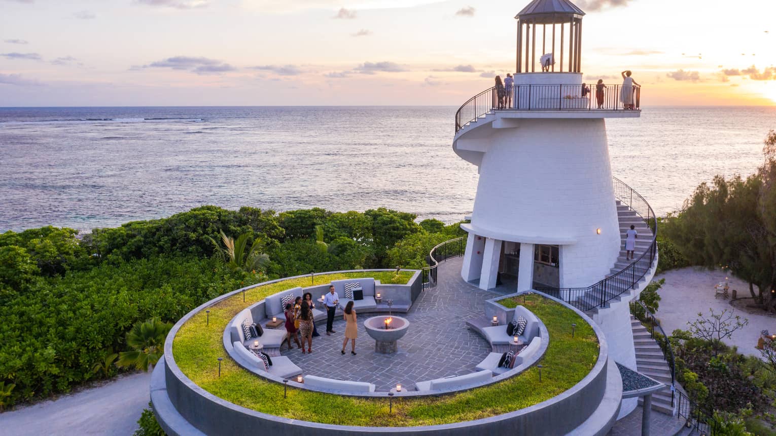 Guests gather on lighthouse spiral stairs, round patio with fire pit at sunset