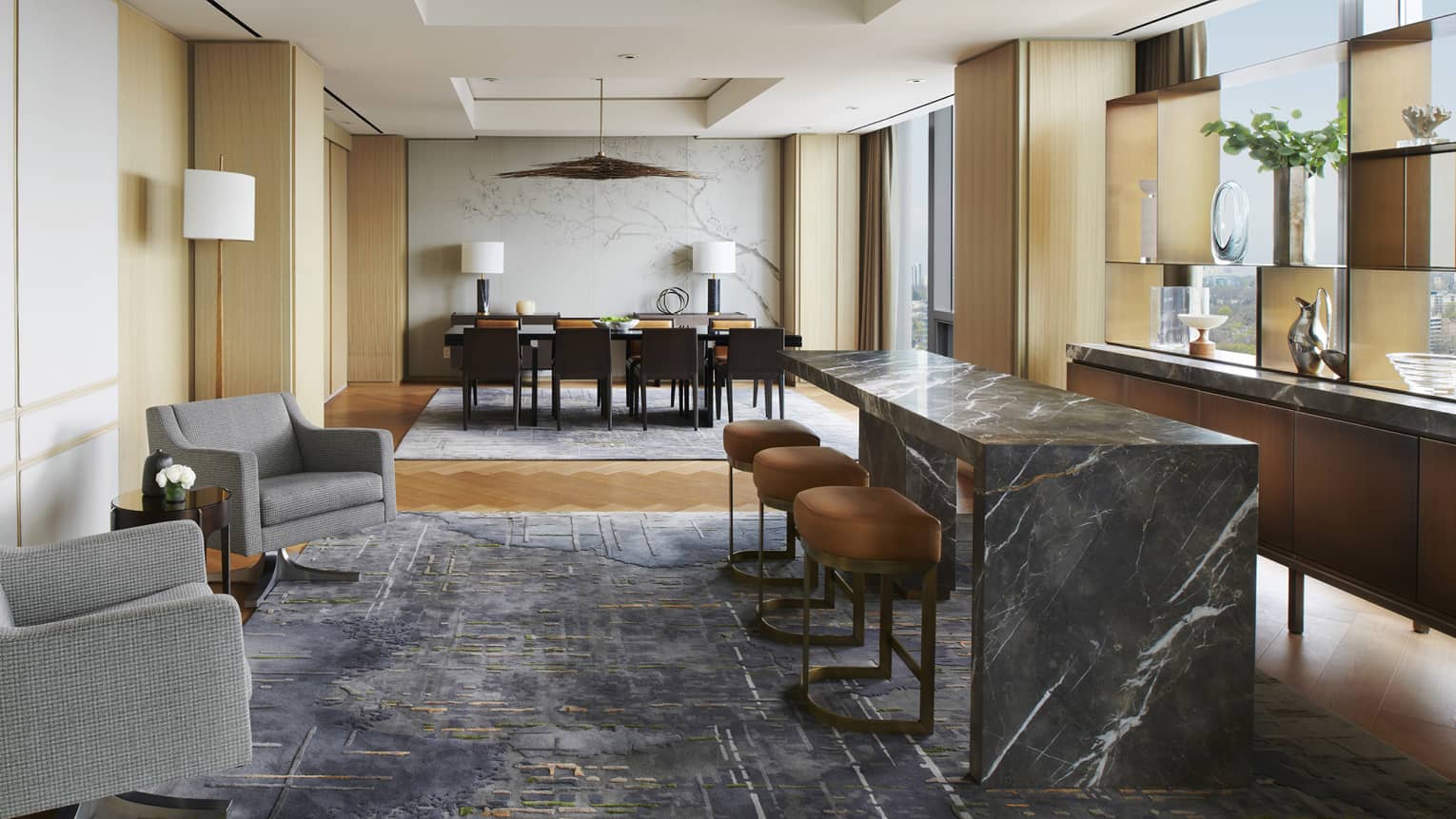 Royal Suite bar and dining area with marbled bar and bar stools, two grey armchairs, rectangular dining table, floor-to-ceiling windows